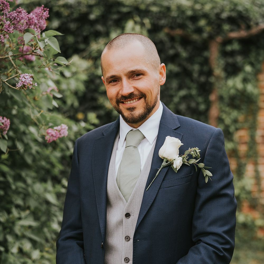 Groom in a blue suit with a grey waistcoat with a white rose buttonhole 