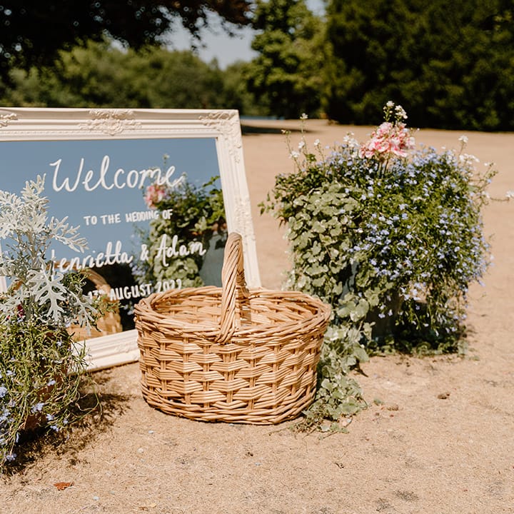 White framed mirror with white writing and wicker basket surrounded by floral bouquets