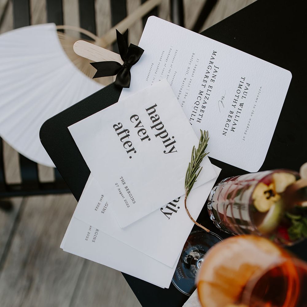 Modern white wedding stationery beside colourful drink