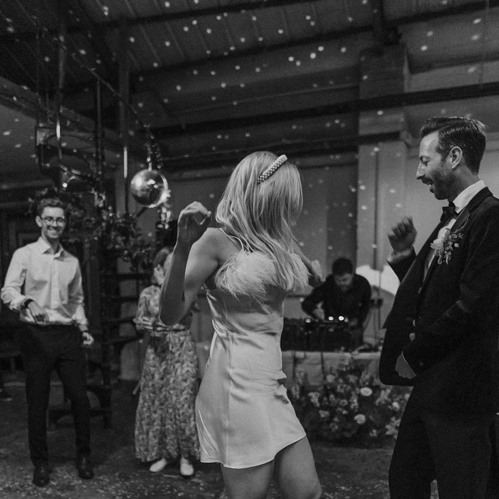 Bride in short white satin dress with feather trimmed neckline dancing with groom in dark tux and bowtie at stylish modern London wedding
