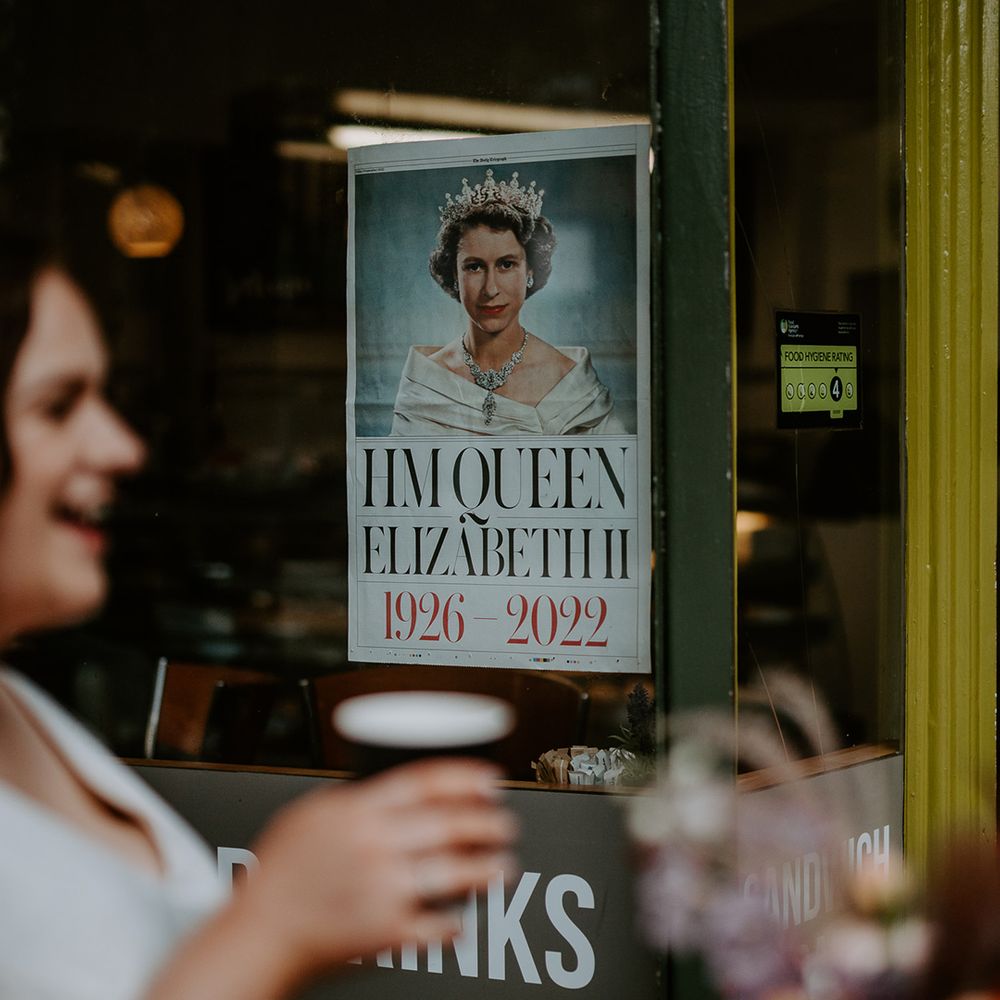 Bride drinks pint at pub wedding venue in London with a poster of Queen Elizabeth II in the background
