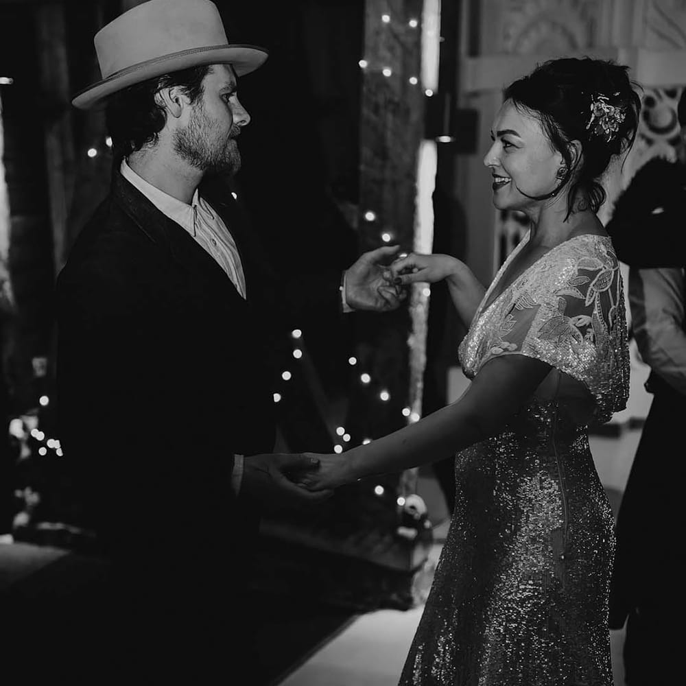 Bride in sequin sparkly reception wedding dress dancing with the groom in a denim suit and hat 