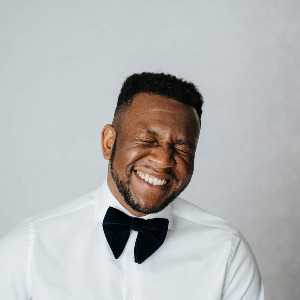 Groom laughing in crisp white shirt and black velvet bowtie 