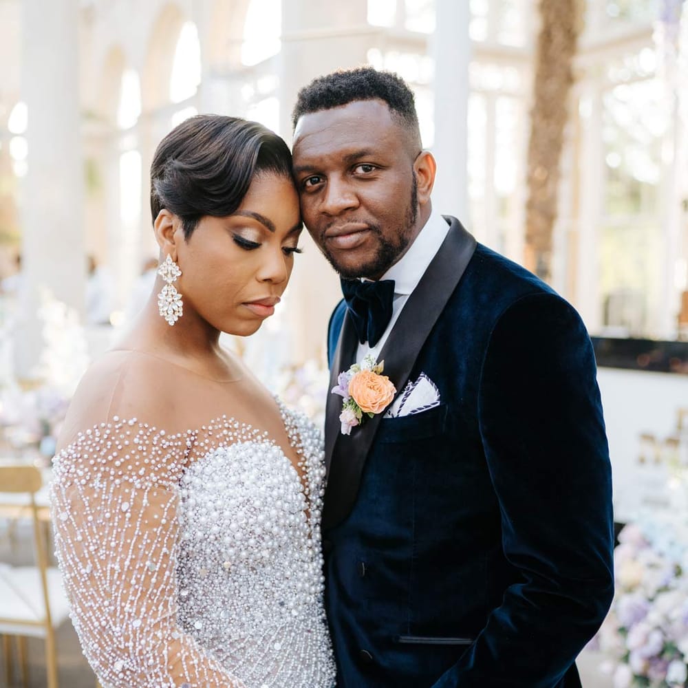 Bride in illusion v neck sheer off shoulder long sleeve pearl embellished wedding gown standing with groom in velvet midnight blue double breasted groom’s blazer, velvet bowtie and peach garden rose boutonniere at vow renewal at Syon Park wedding venue