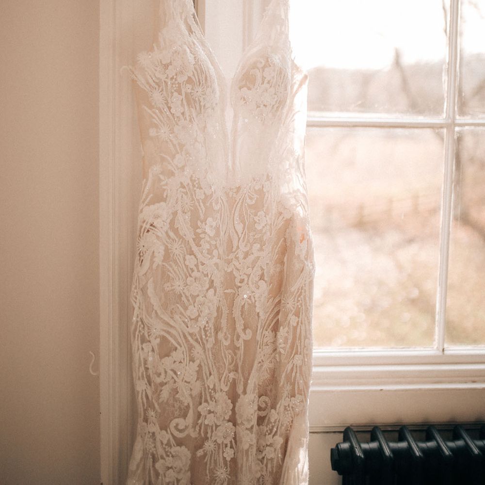 Lace embellished wedding dress hanging on white coat hanger at Aswarby Rectory 
