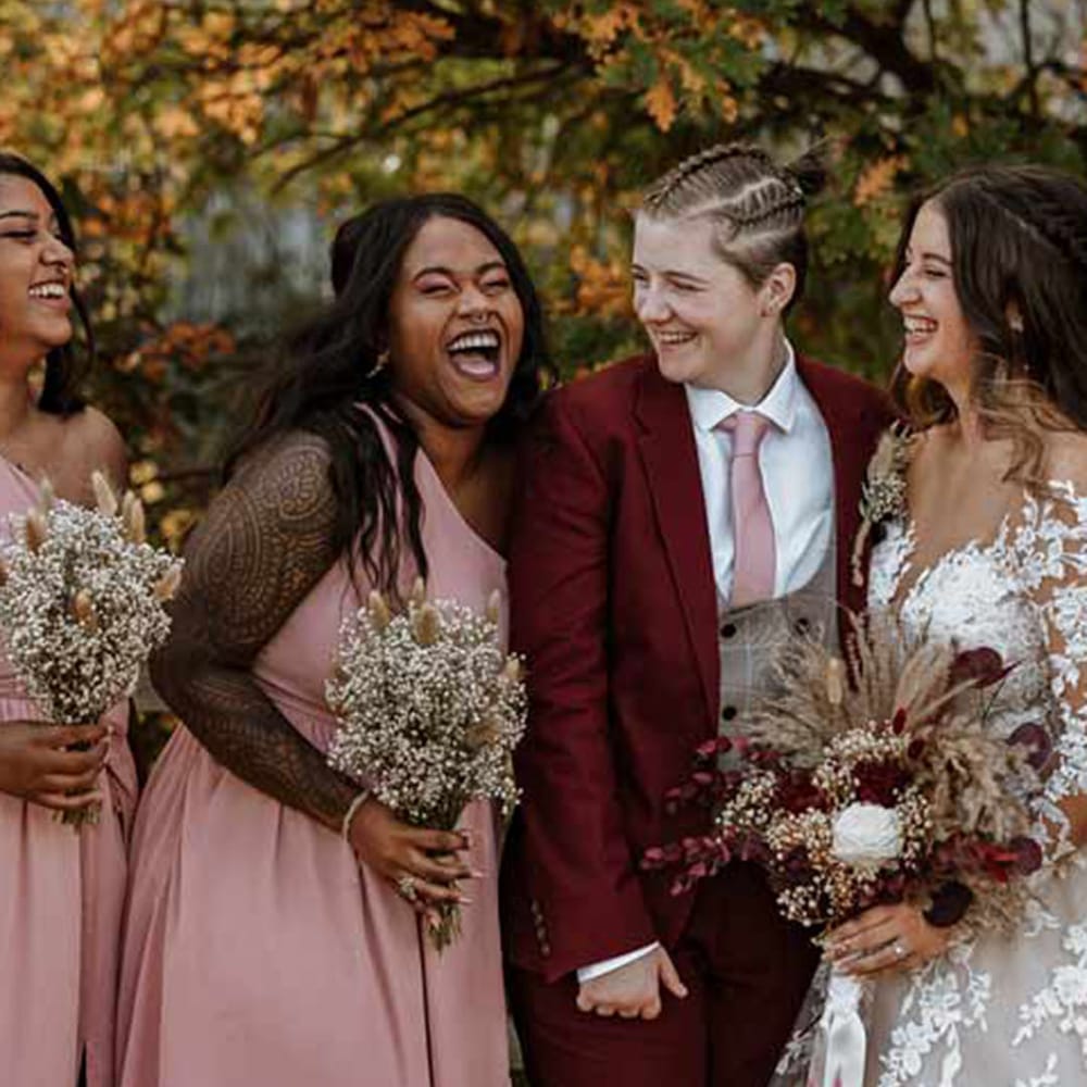 Dusky pink bridesmaid dresses with two brides in illusion lace wedding dress and a burgundy suit 