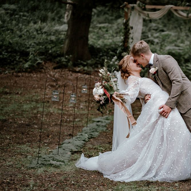 Bride and groom kissing in the woods with votive candles lining the aisle 