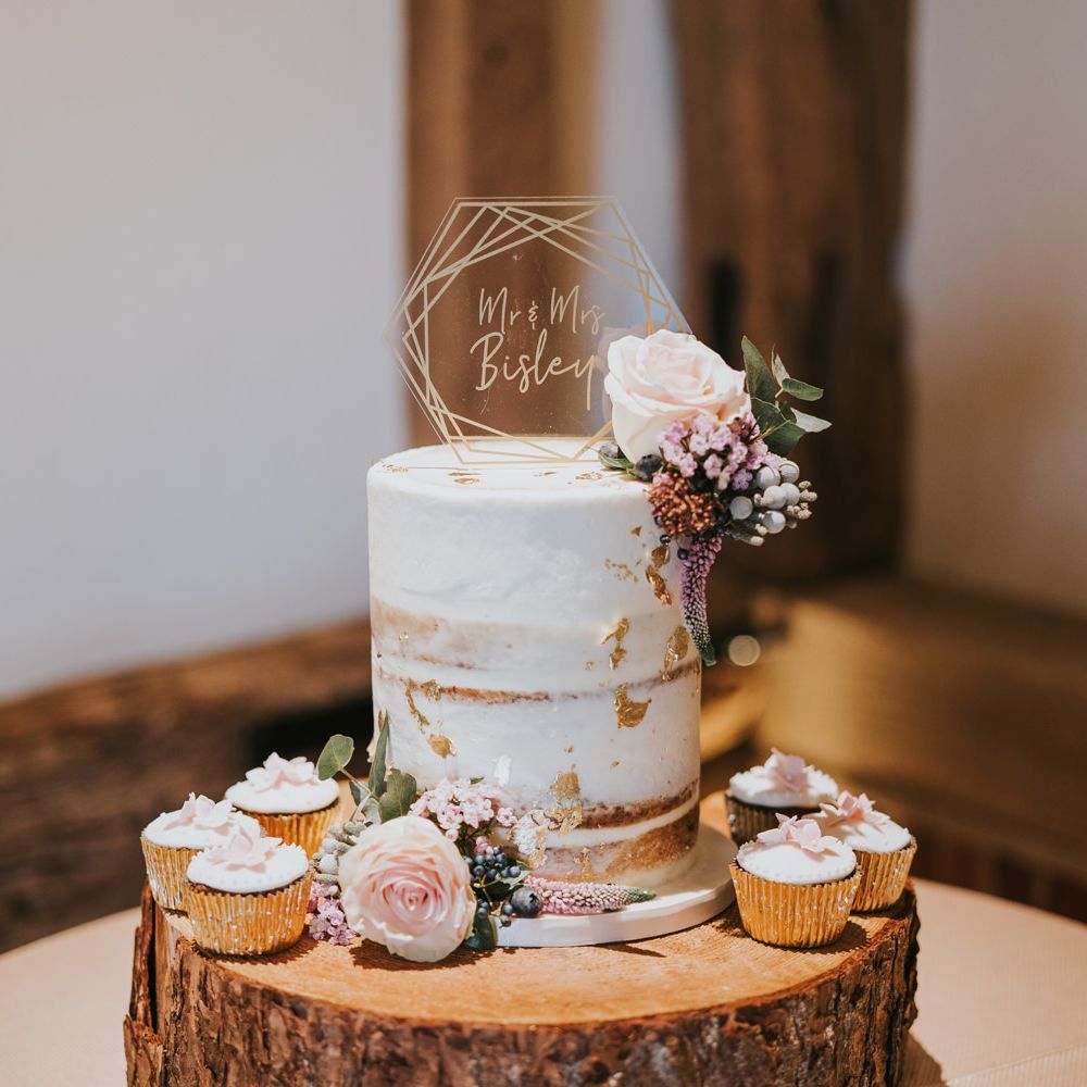 Naked cake upon tree trunk surrounded by cupcakes