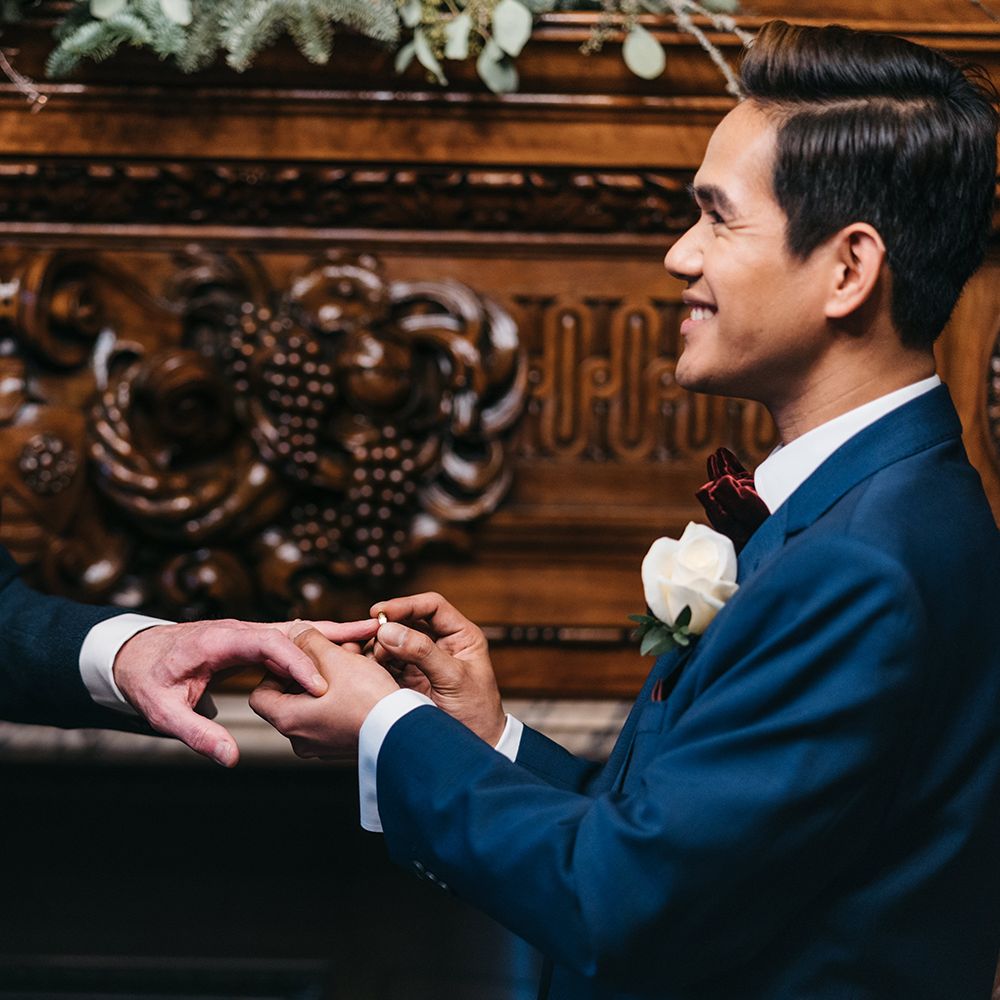 Groom places ring on grooms finger during wedding ceremony
