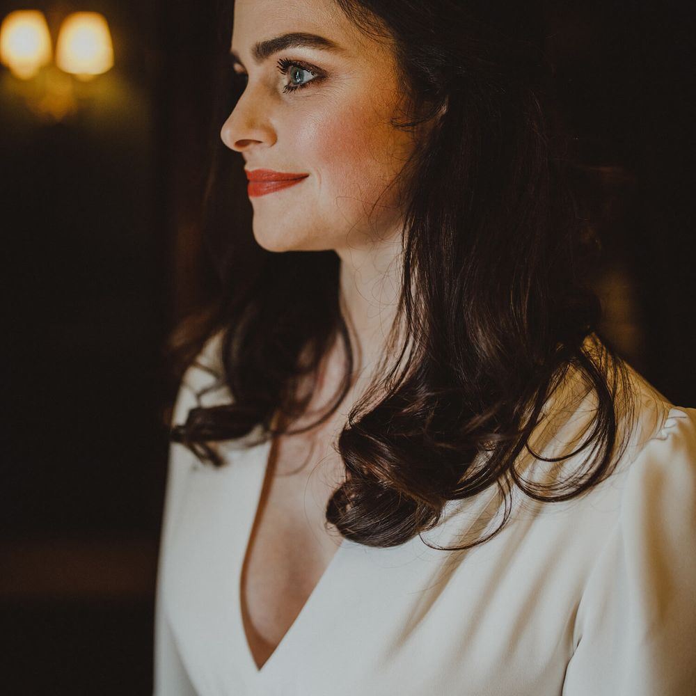 Close up shot of bridal makeup, bride has dark hair with peachy red lipstick and loosely curled hair with sparkling hair accessory 
