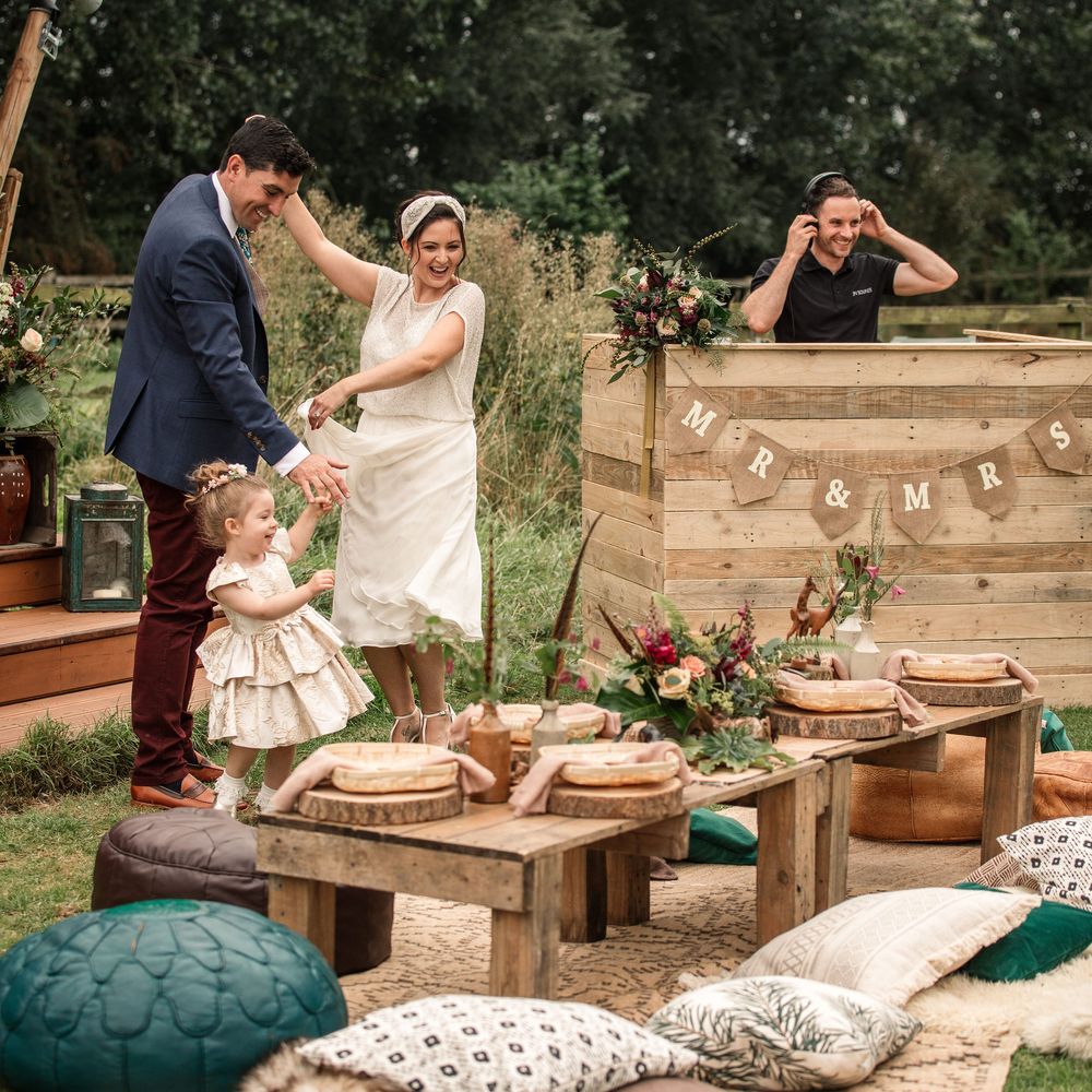 Bride & groom dance outdoors with DJ in wooden booth