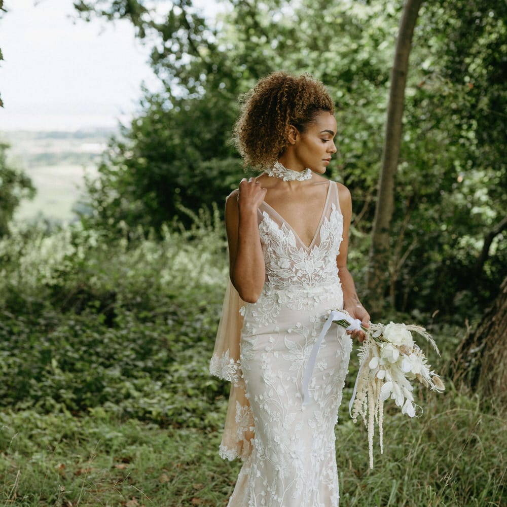 Boho bride in the woods at Berwick Lodge wearing floral lace embroidered wedding dress with plunge neckline and tulle bridal cape with lace edged detail