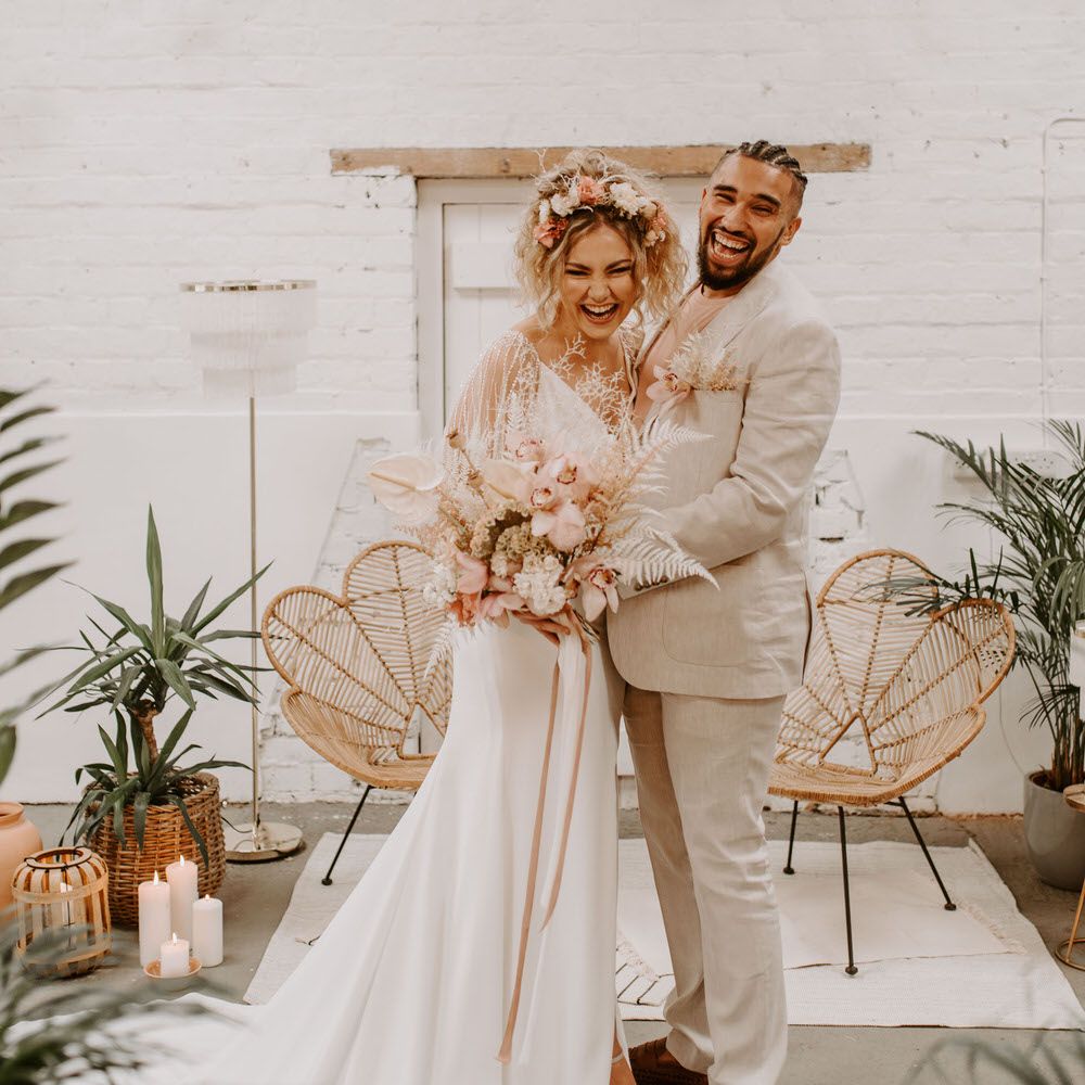 Bride and groom at tropical wedding altar with pink and white florals and a cream suit