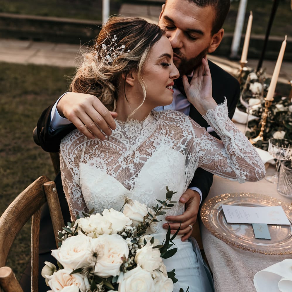 Bride in a lace bodice wedding dress with long sleeves holding an all white rose wedding bouquet 