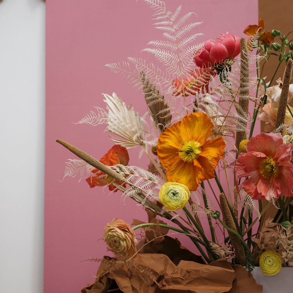Pink, orange and dried flower bouquet in front of a dusty pink background