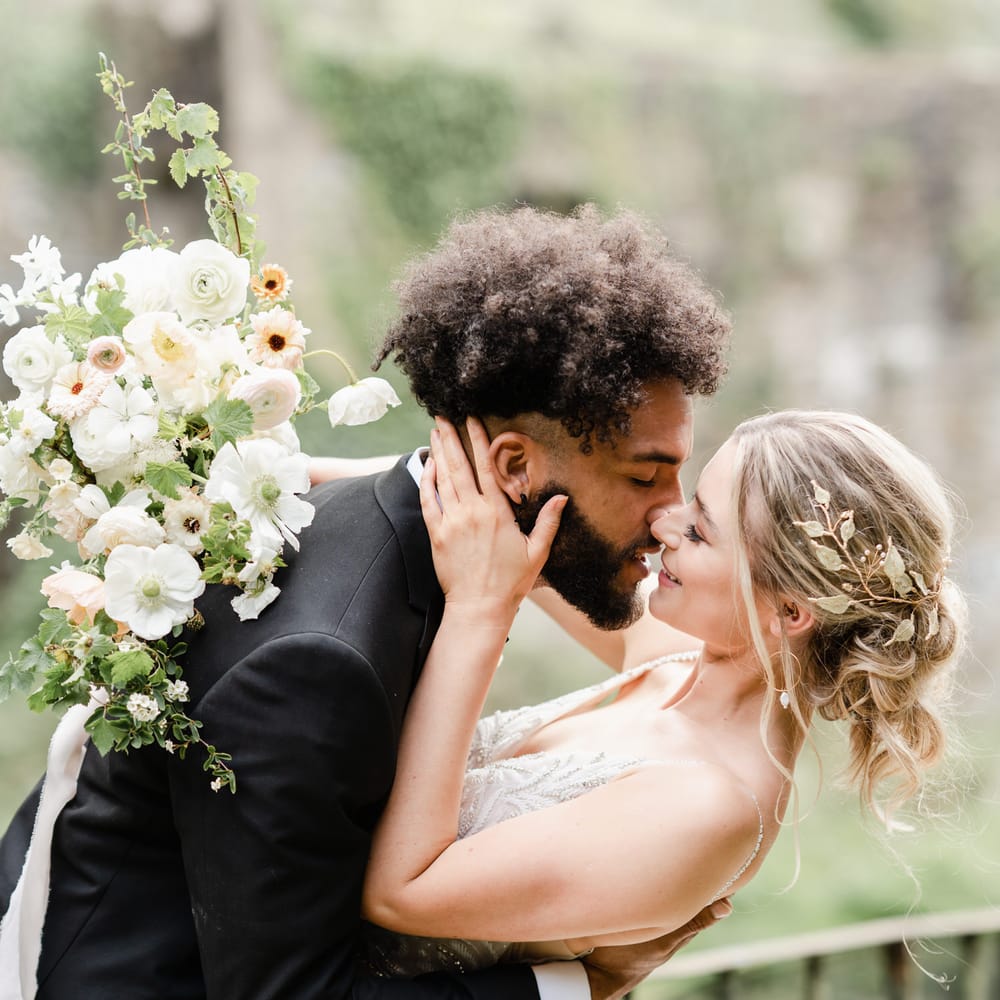 Groom in a black tuxedo leaning his bride over for a kiss with a loosely pinned up do