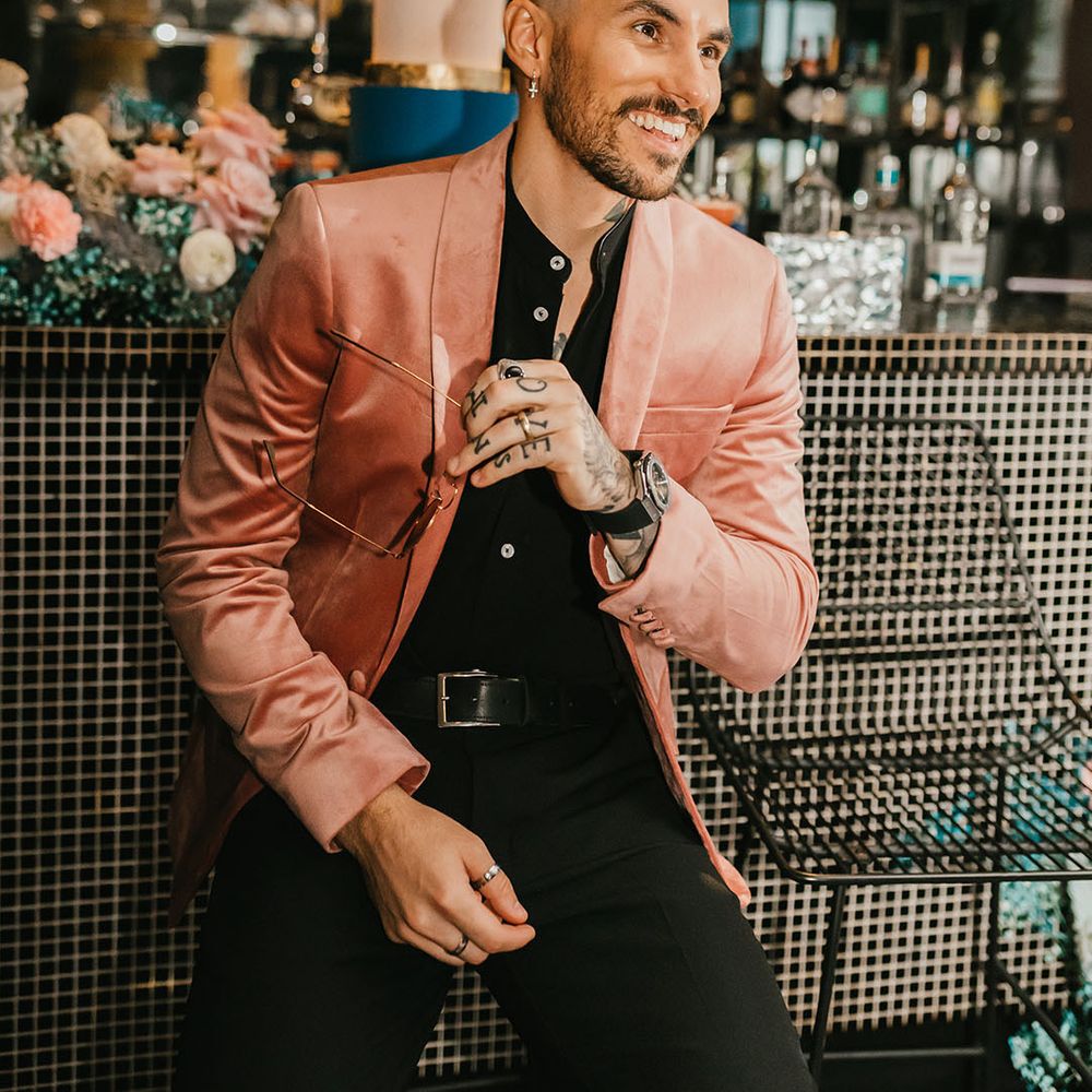 Stylish groom in a black shirt and pink velvet jacket sitting at the bar 