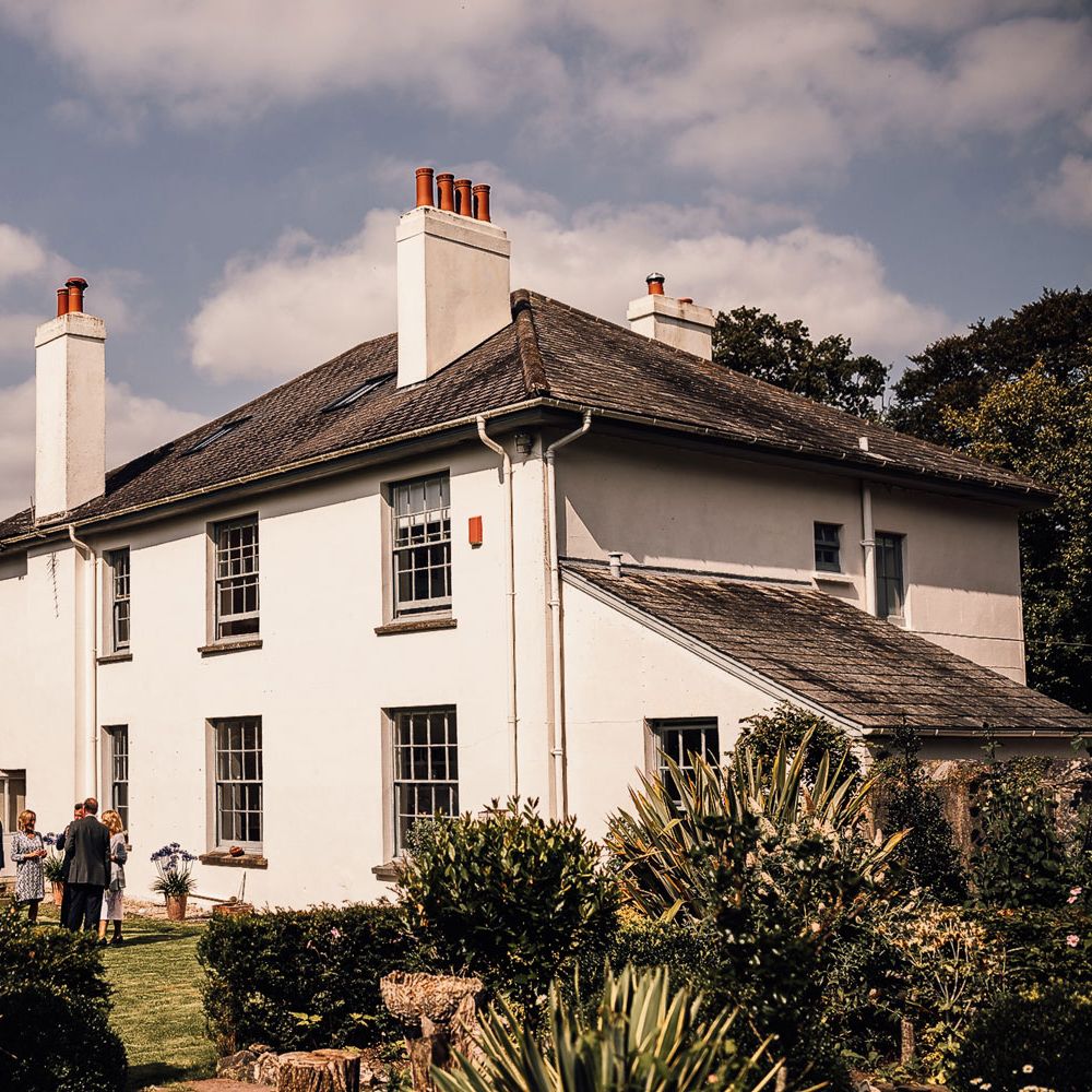 Exterior of white house in Cornwall with wedding guests in garden for wedding