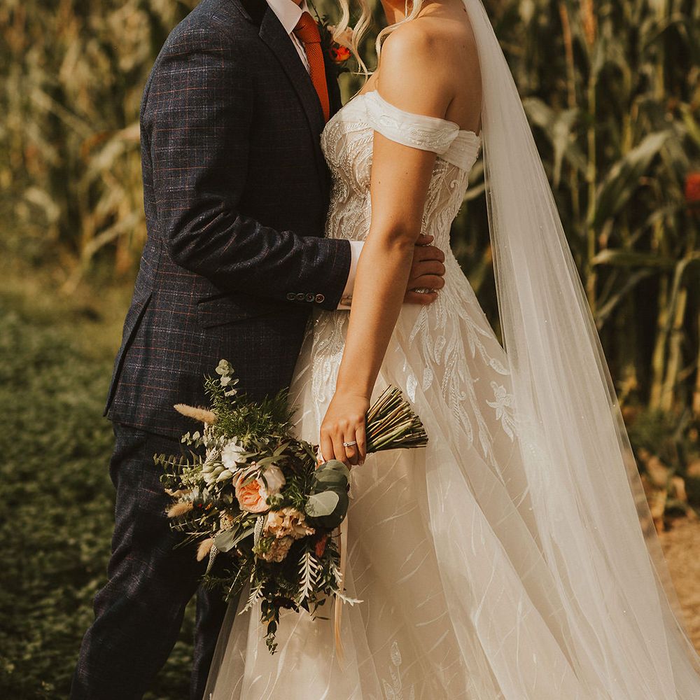 Groom kisses his bride in off the shoulder wedding dress clutching bouquet 