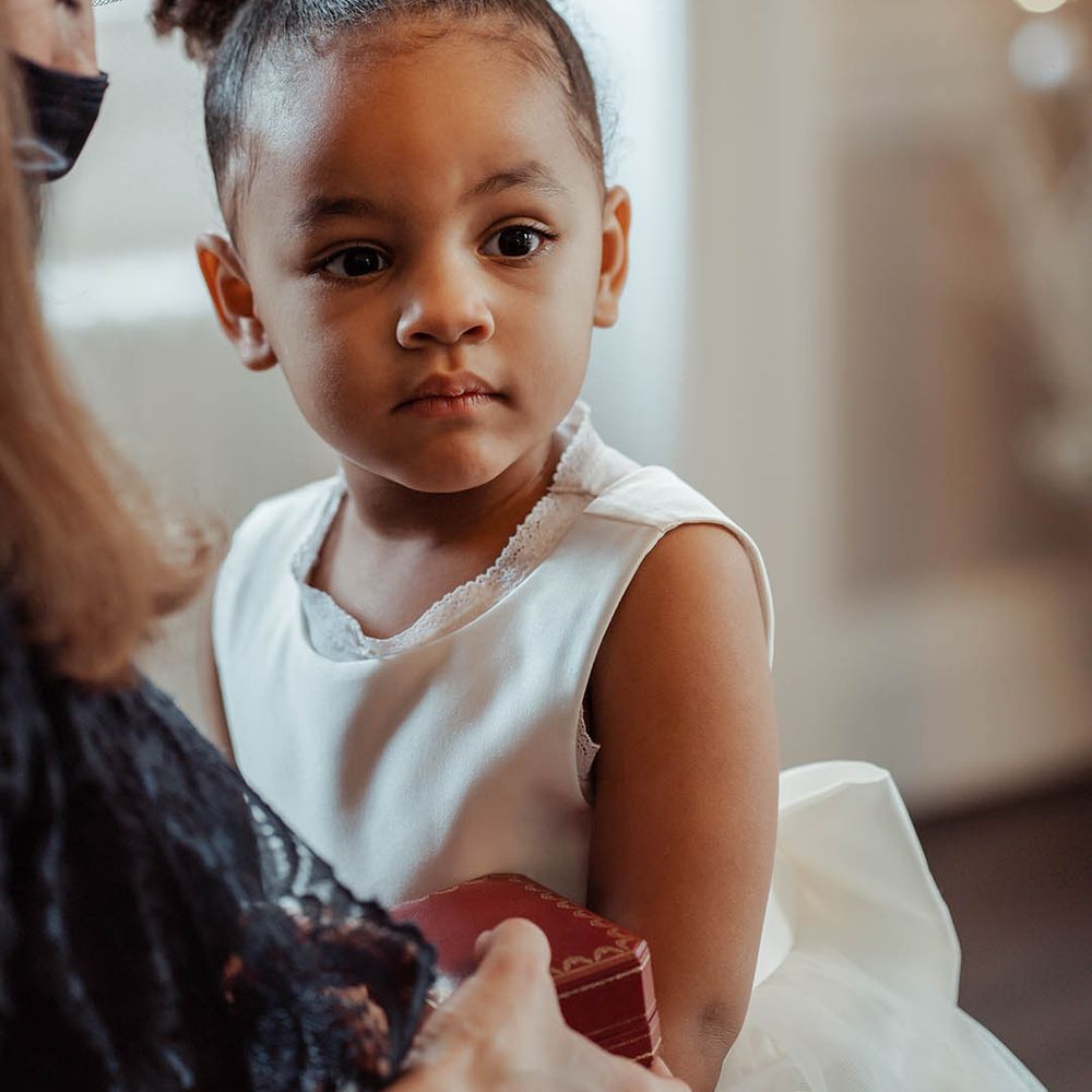 Flower girl wears hair in a bun and white tea length dress