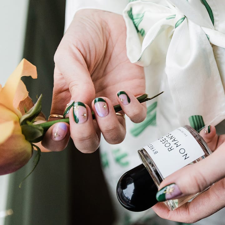 Bride has green and purple wedding nails with gold stars holding perfume and flower