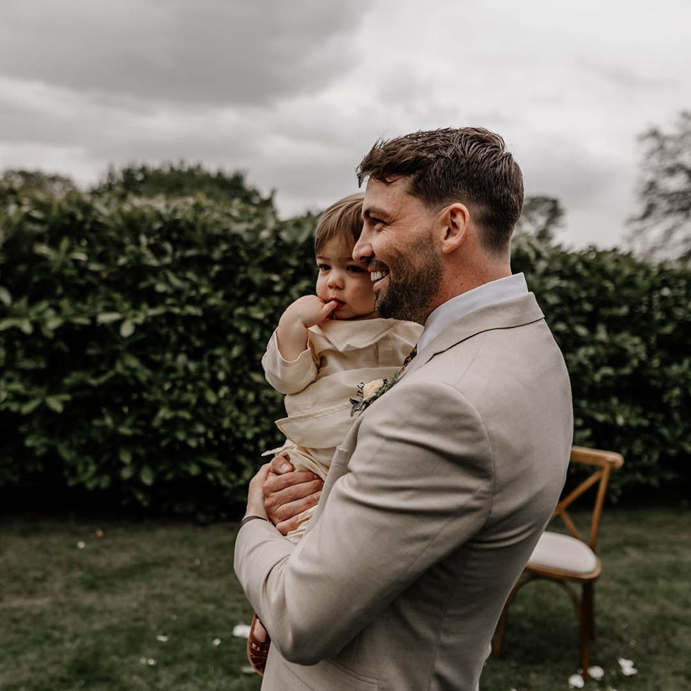Groom in a beige suit holding his son at the altar 