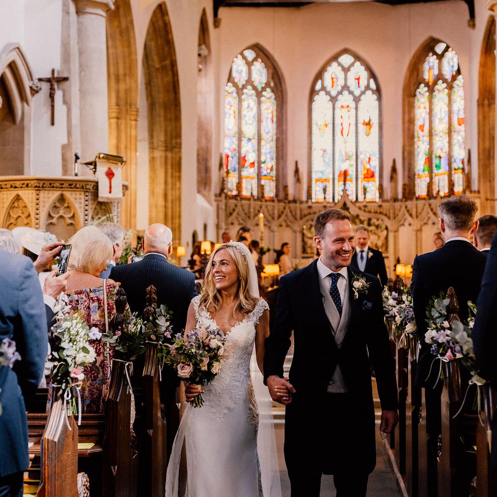 Bride and groom smile at their wedding guests as they walk back down the aisle as a married couple 