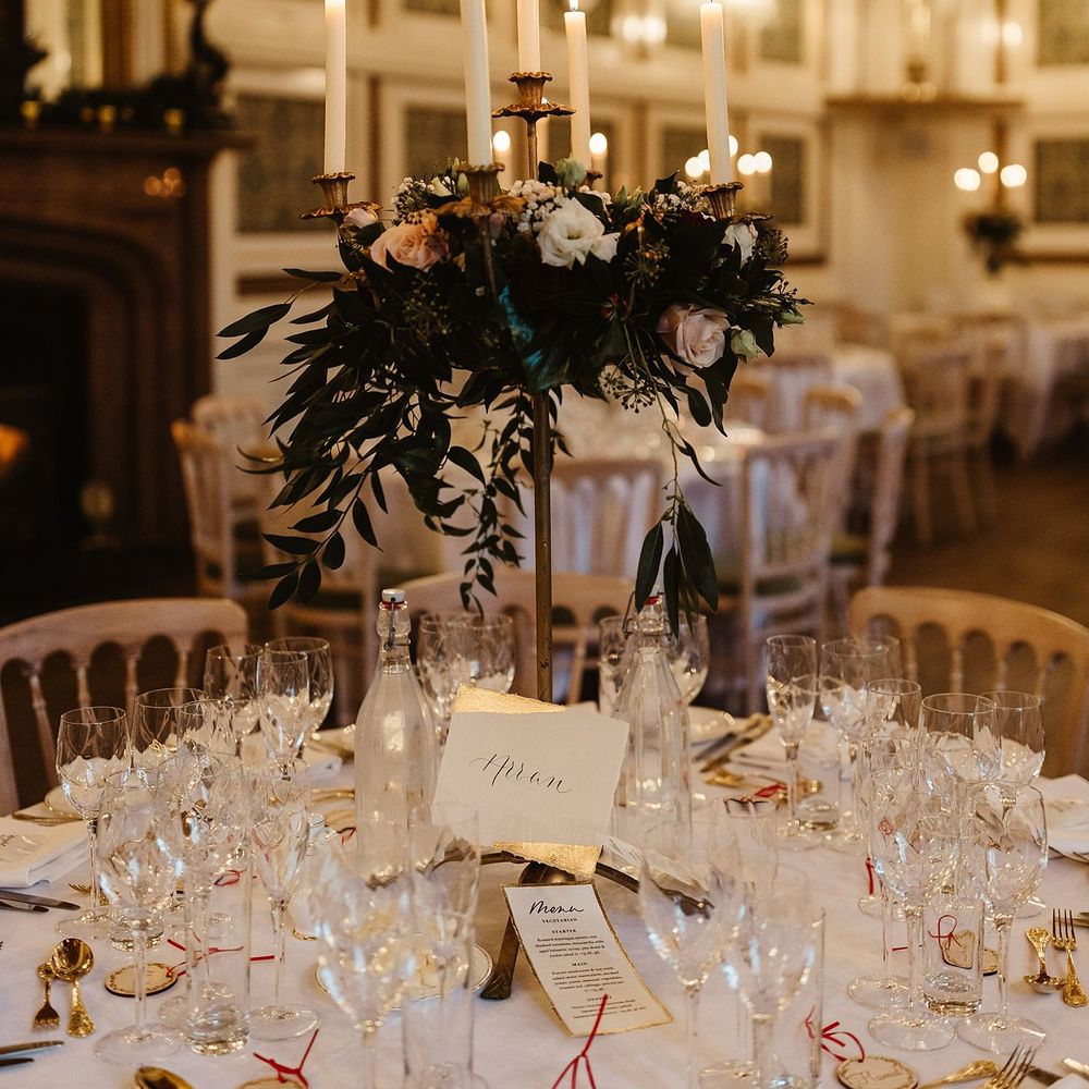 Wedding reception tablescape complete with white tablecloths and floral bouquets set up on gold candle pillars 