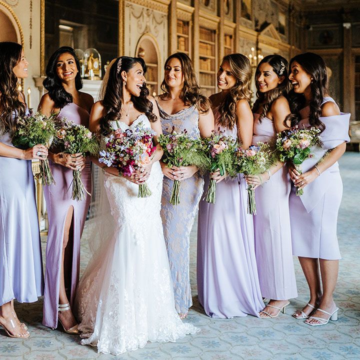 Bride stands with her bridesmaids wearing lavender bridesmaid dresses and holding brightly coloured floral bouquets 