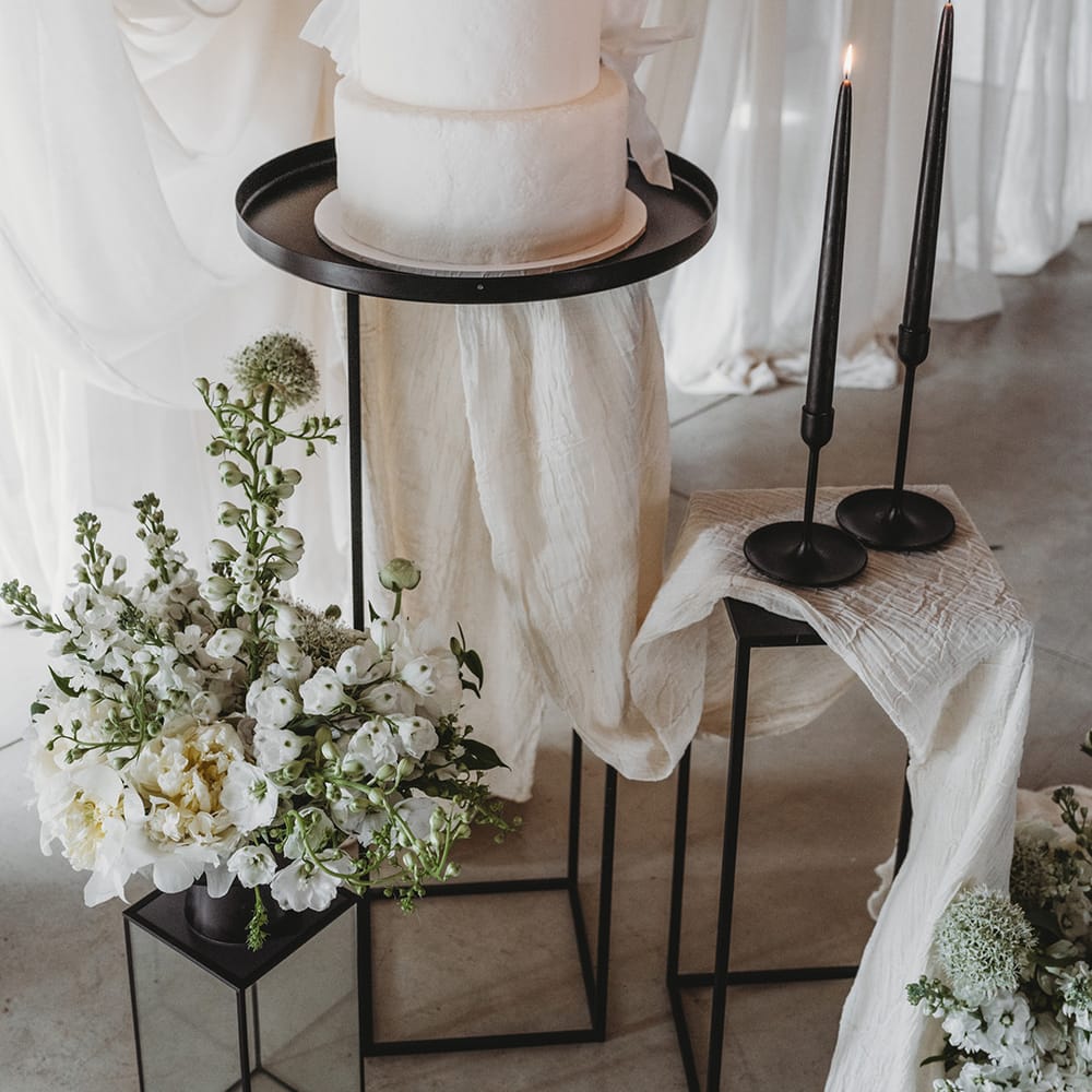 Three tier white iced vegan wedding cake with black taper candles and wedding drapes