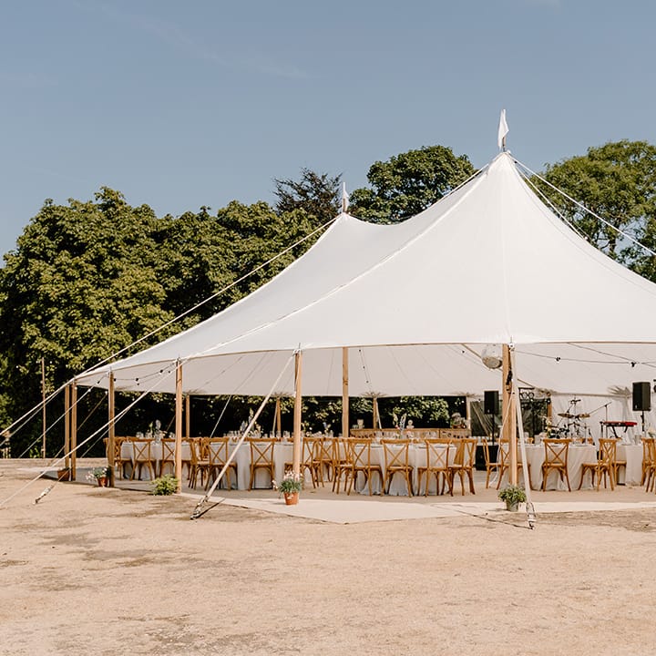 Outdoor wedding tent for summer wedding with pastel florals and wooden chairs 