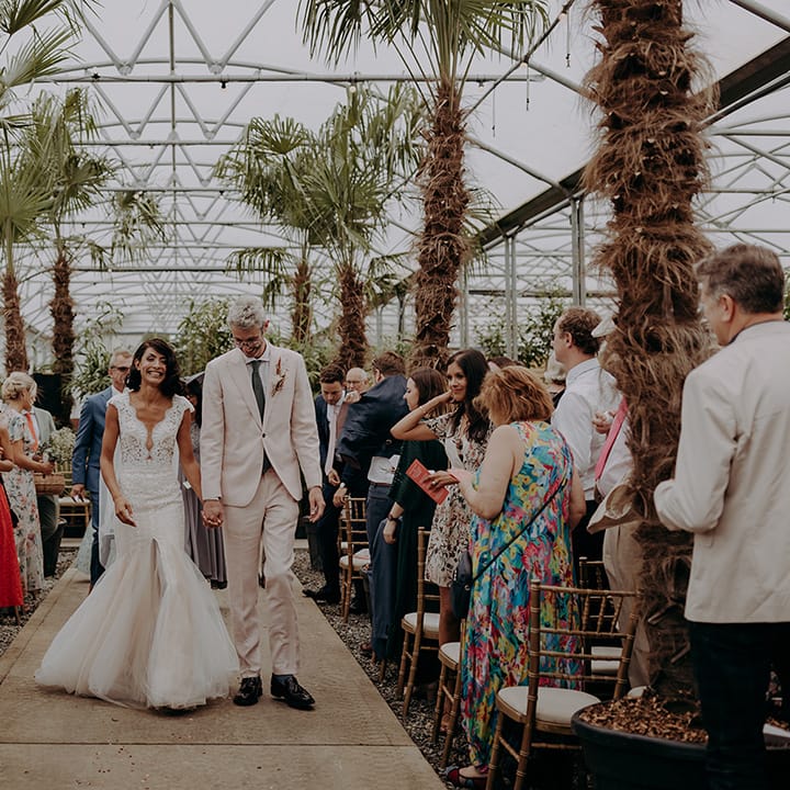 Bride and Groom walk up the palm tree lined aisle smiling and holding hands