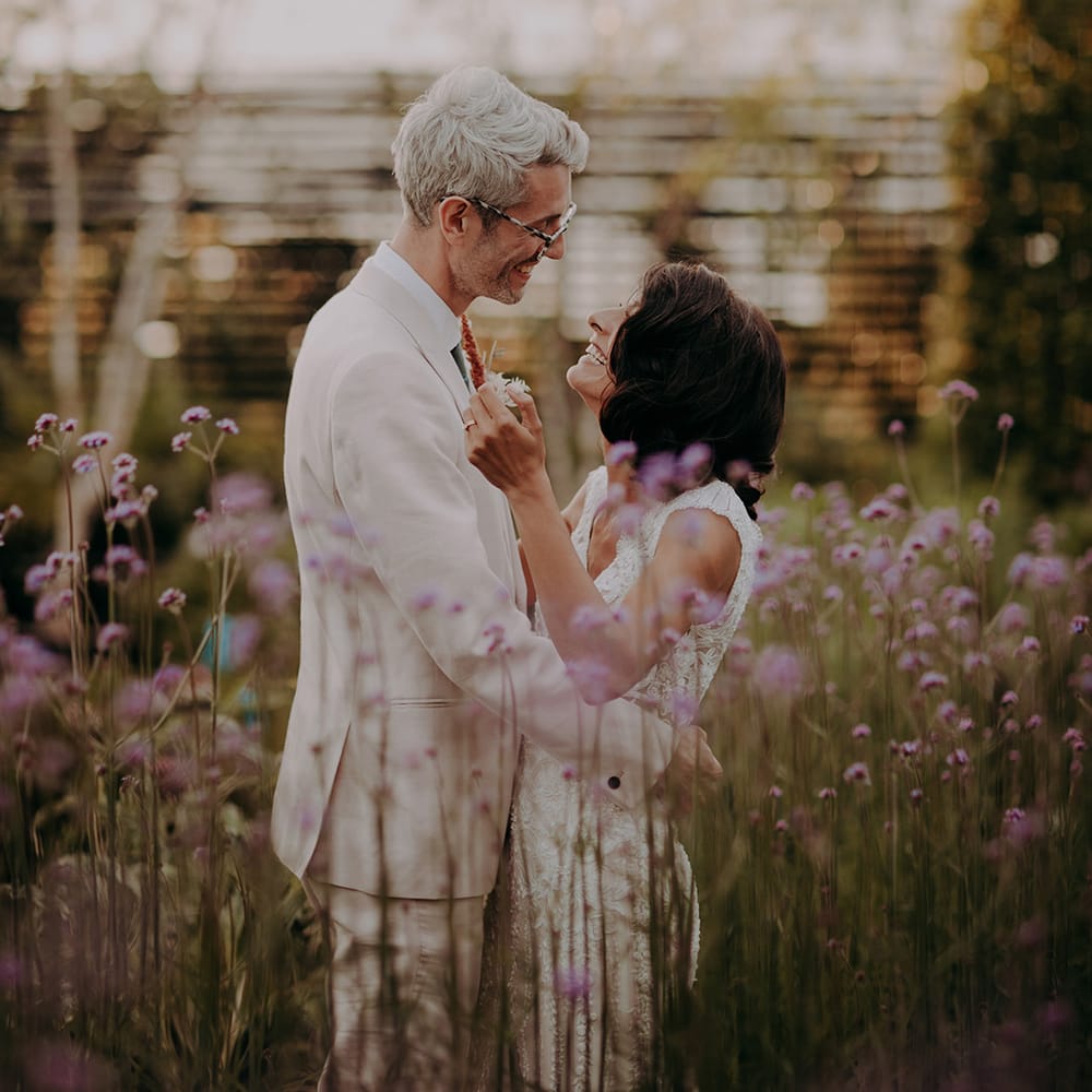 Bride and Groom holding each other and laughing in a field of tall purple flowers