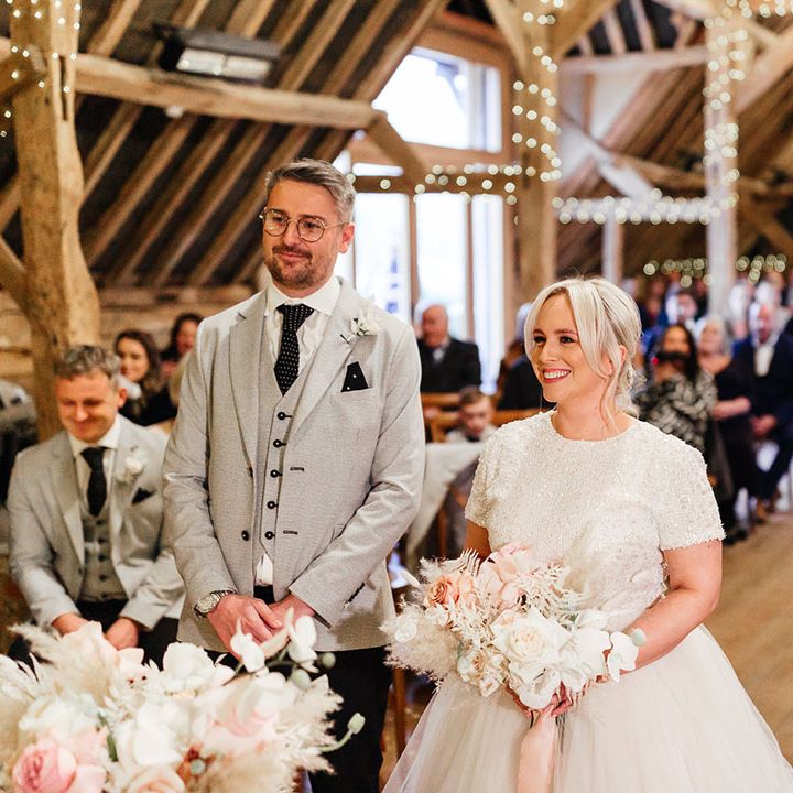 Fairy lit barn wedding venue in Hampshire with the bride and groom standing at the altar for their ceremony 