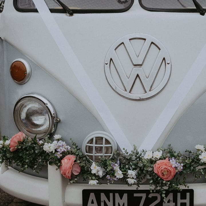 The VW camper van wedding car decorated with white ribbon and pink flowers on the bumper 
