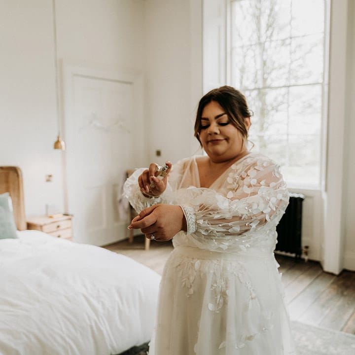 Bride in All Who Wonders lace wedding dress spraying on wedding scent perfume 