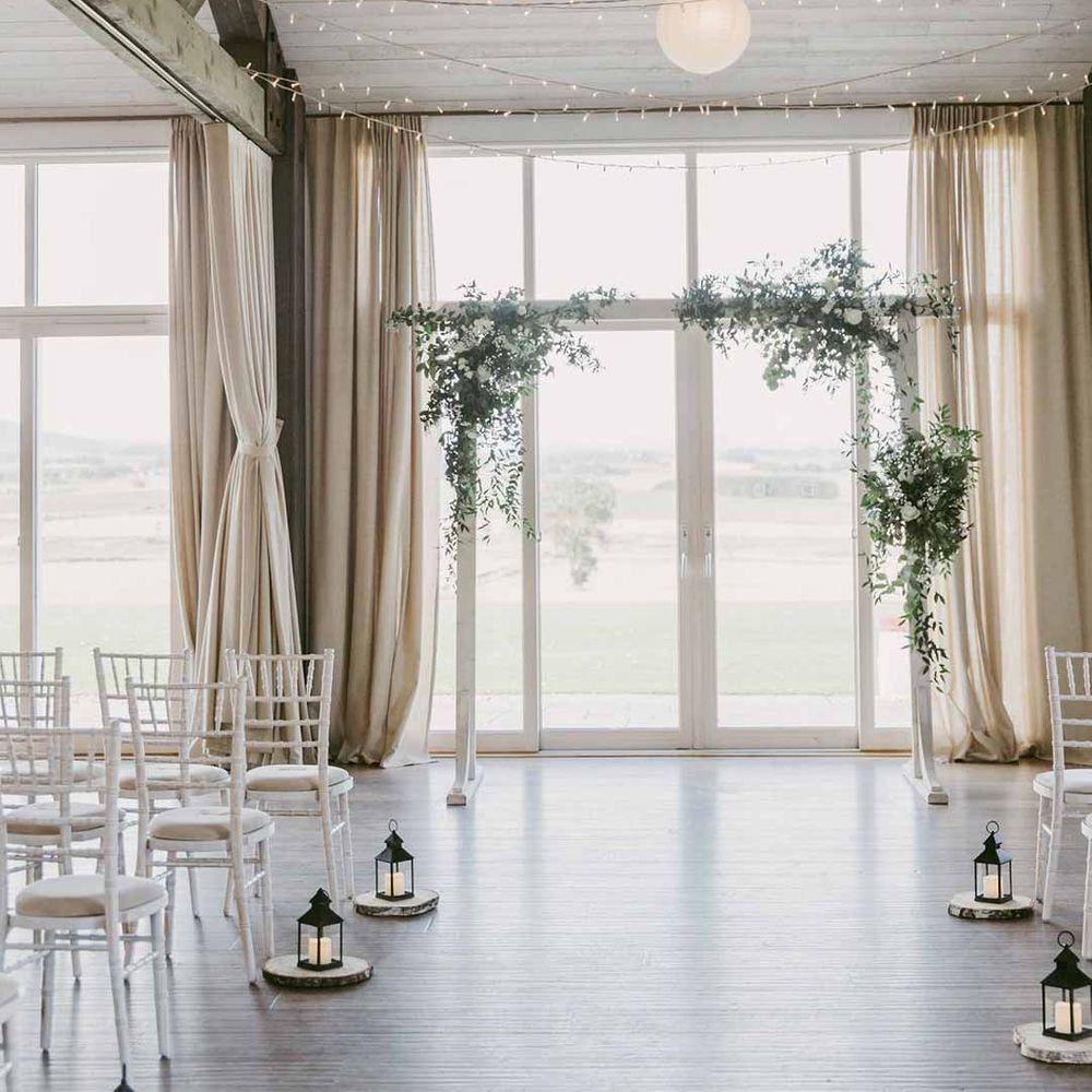 Wedding reception room of Barra Castle wedding venue Scotland with fairy lights, white wooden wedding arch, foliage arrangements and aisle candles 