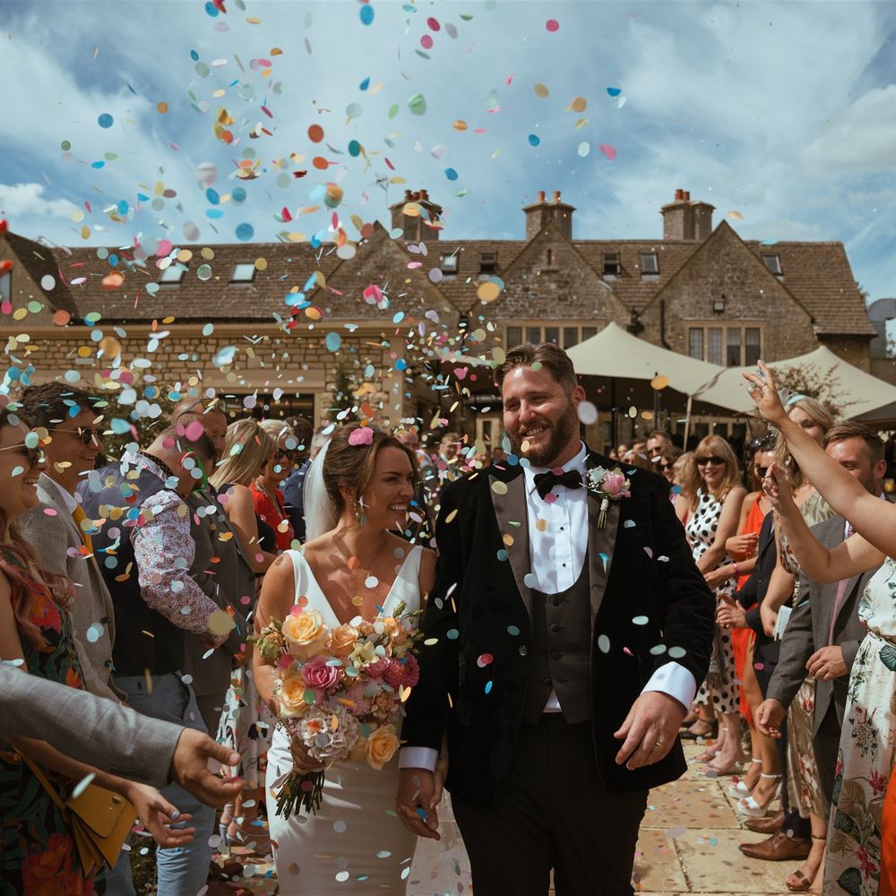 Colourful wedding confetti fluttering down over the bride and groom at their outdoor wedding 