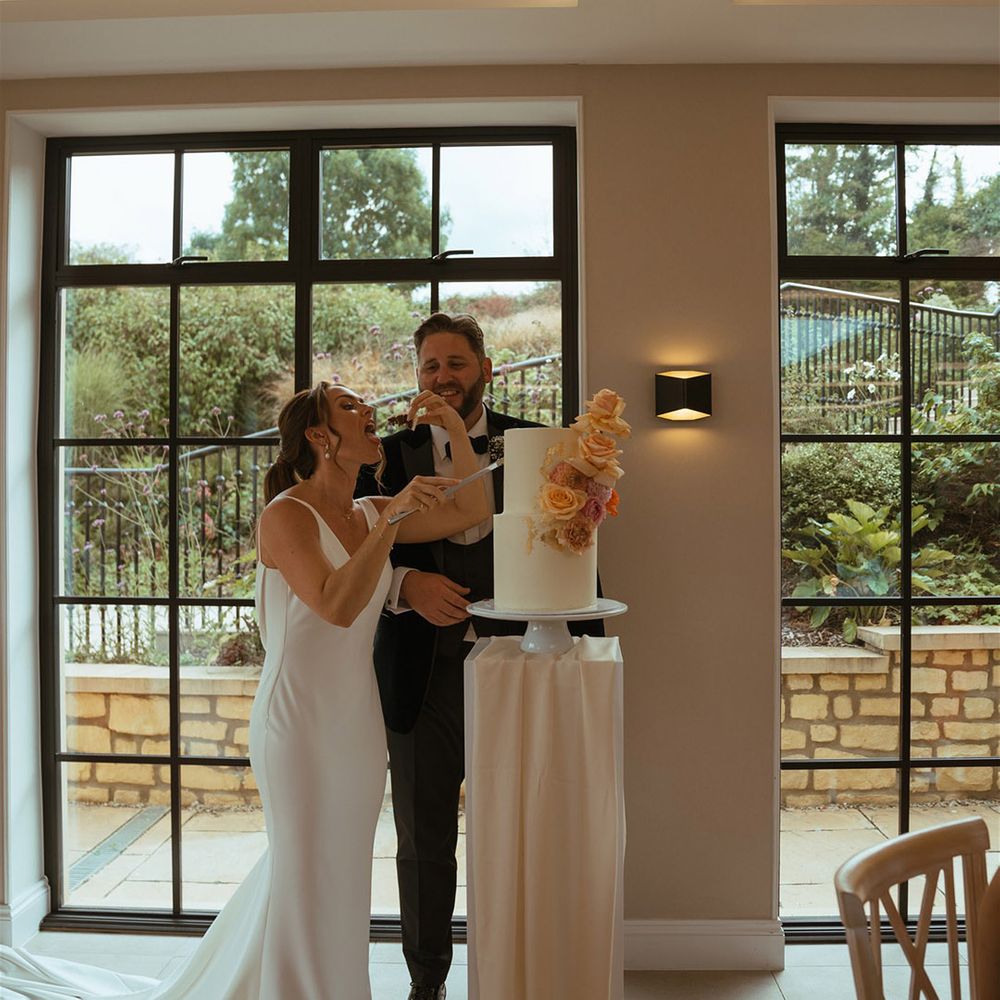 Bride and groom cut the two tier white frosted wedding cake decorated with pink and orange roses 