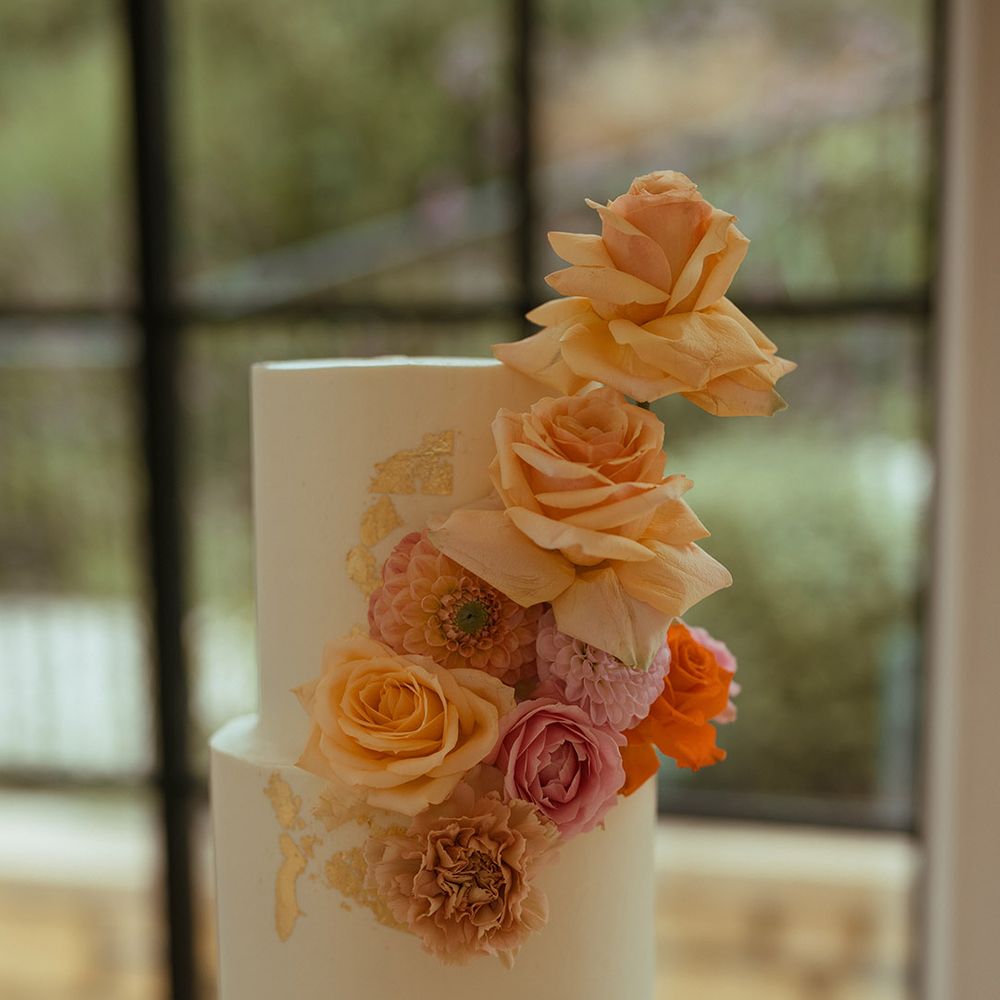 Two tier white frosted wedding cake decorated with pink and orange rose cake decorations