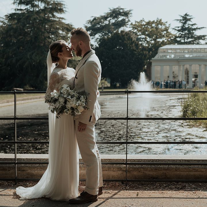bride and groom portrait in front of Gunnersbury Park wedding venue in a long sleeve wedding dress and beige suit 