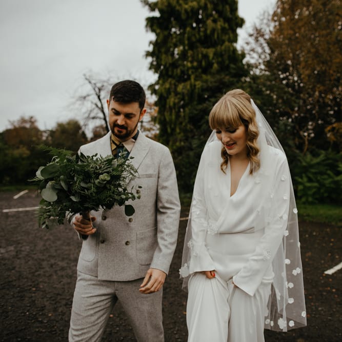 Groom in a grey double breasted suit holding the brides green foliage wedding bouquet