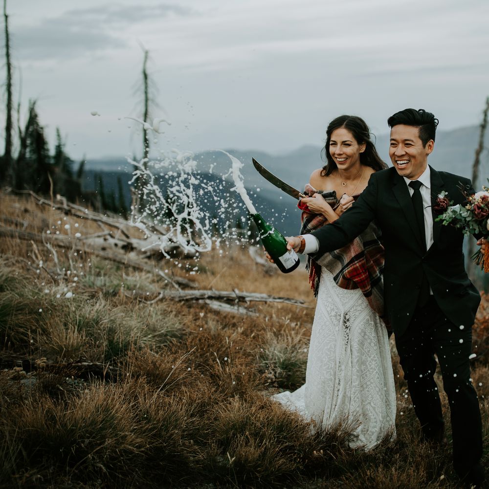 Bride & groom sabre champagne bottle on mountain top 