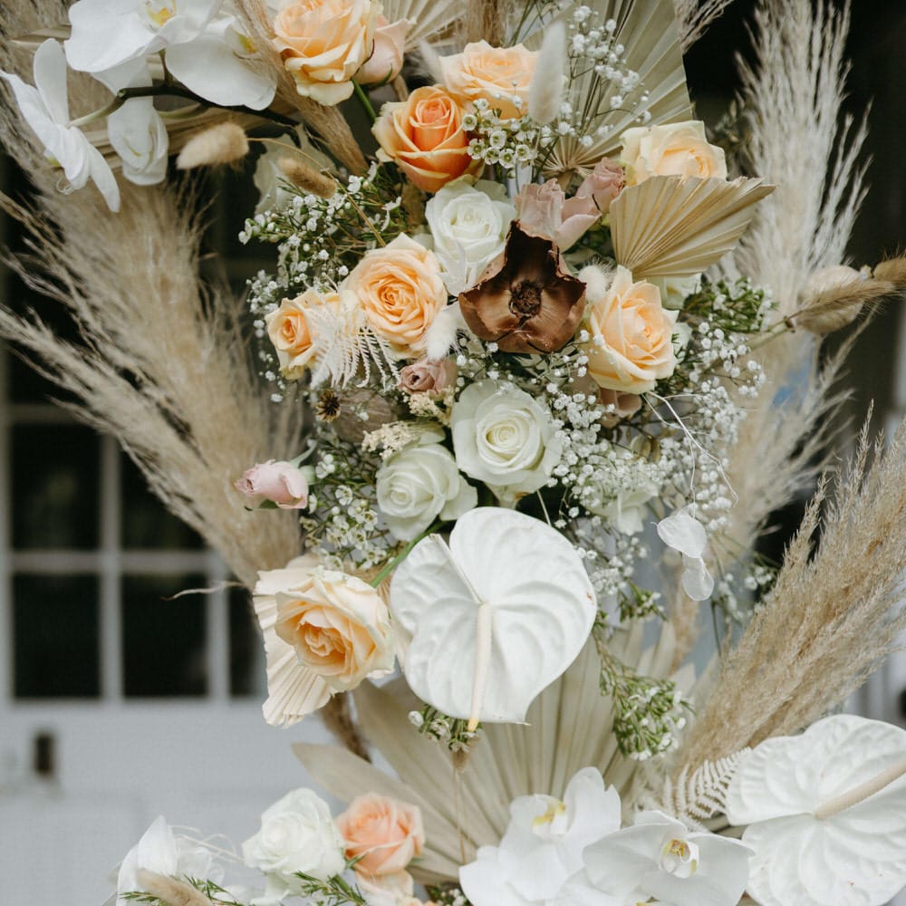 Flower arch detail of dried palms, pampas grass, white anthuriums, roses and orchids