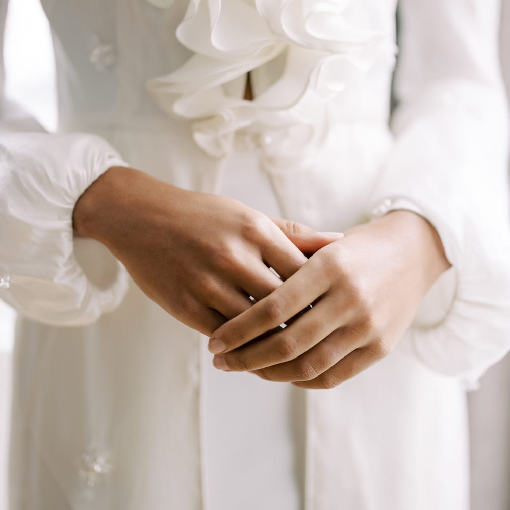 Bride clasps hands together whilst wearing long sleeved bridal gown with full sleeves and ruffled front
