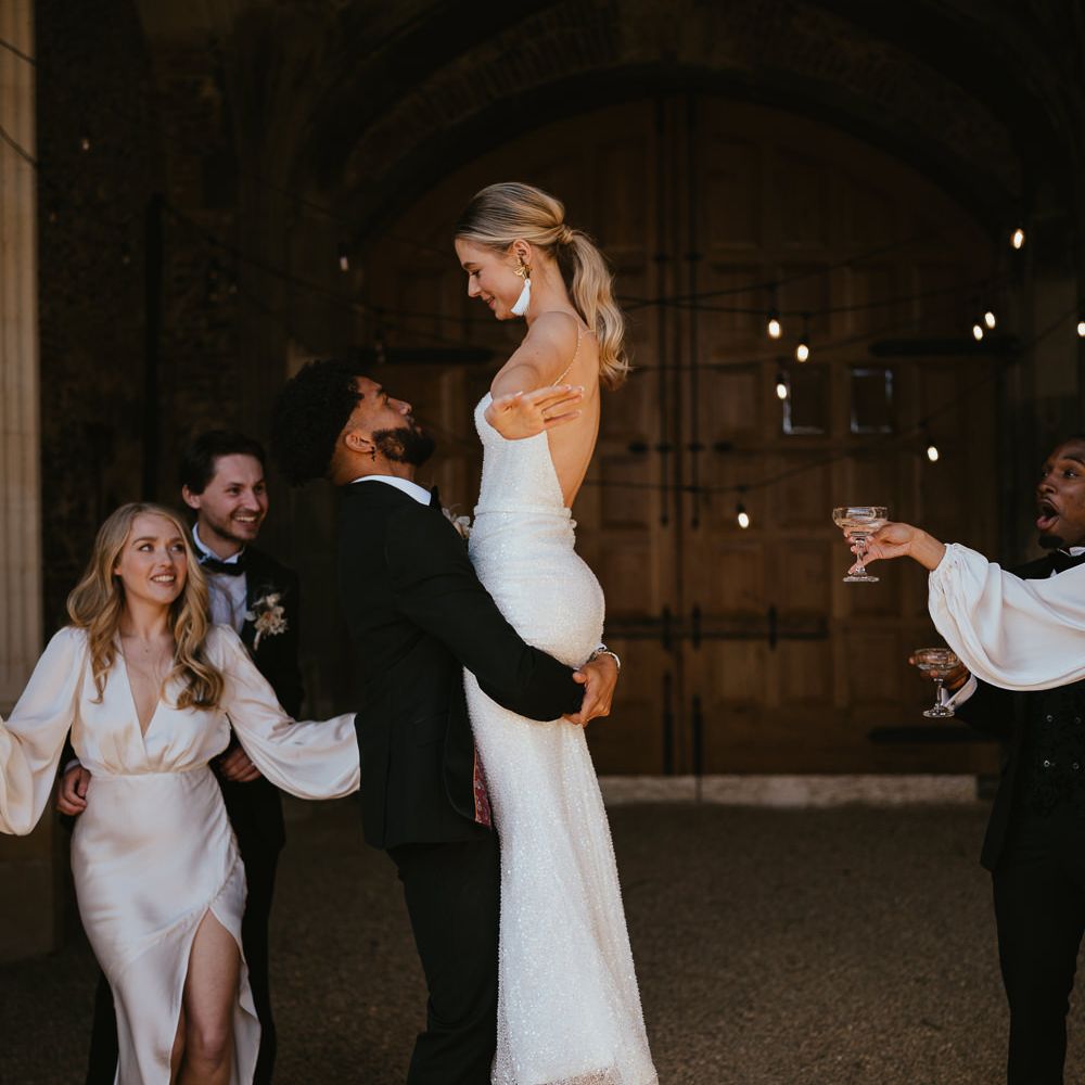 Groom in a tuxedo picking up his bride in a fitted sparkly wedding dress at Pentney Abbey Estate