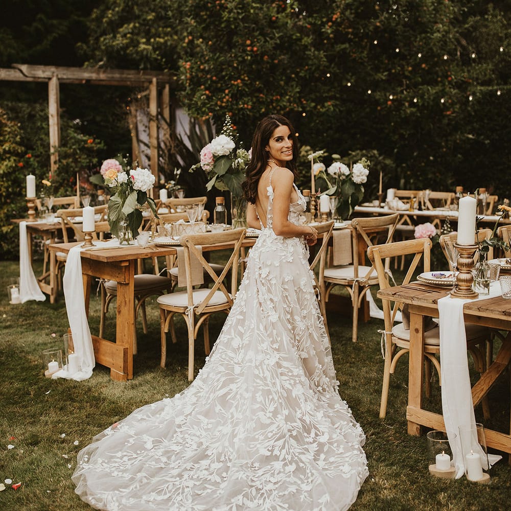 Bride stands beside table on her wedding day wearing Alena Leena Bridal gown