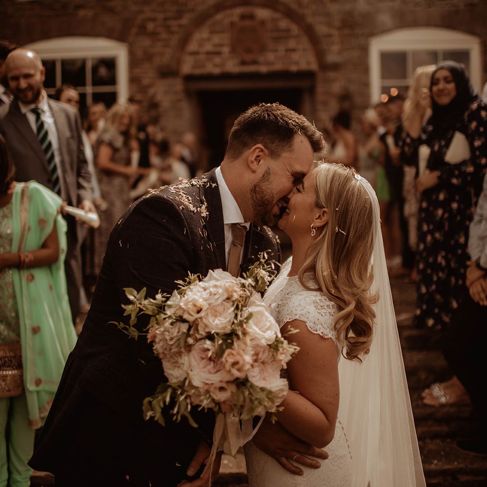 Confetti moment at Dewsall Court with bride in a lace cap sleeve wedding dress holding a pink rose bouquet 