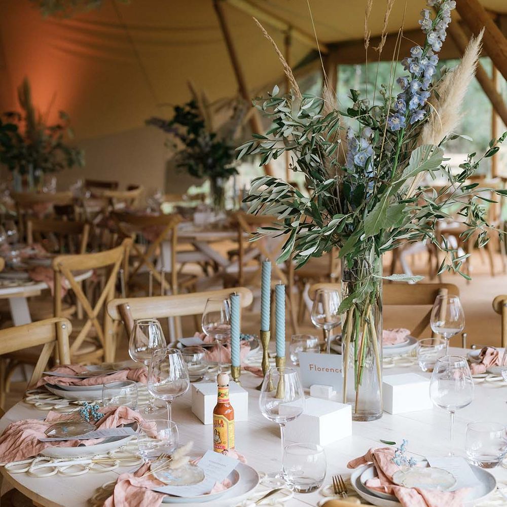 Pastel themed tables cape with twisted blue candles, gold and silver accents, pink napkins, tall dried flower centrepiece
