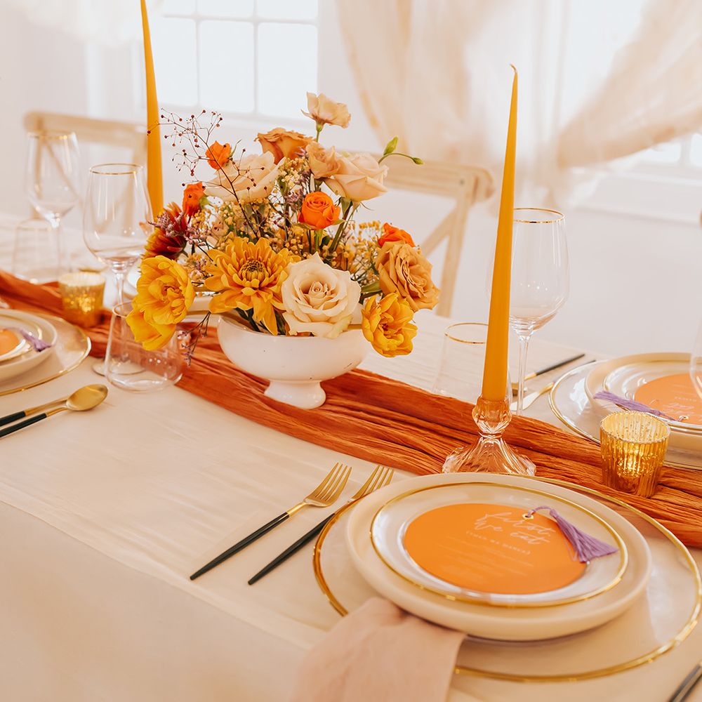 Elegant place setting with orange table runner, taper candles and menu card on gold rimmed plates